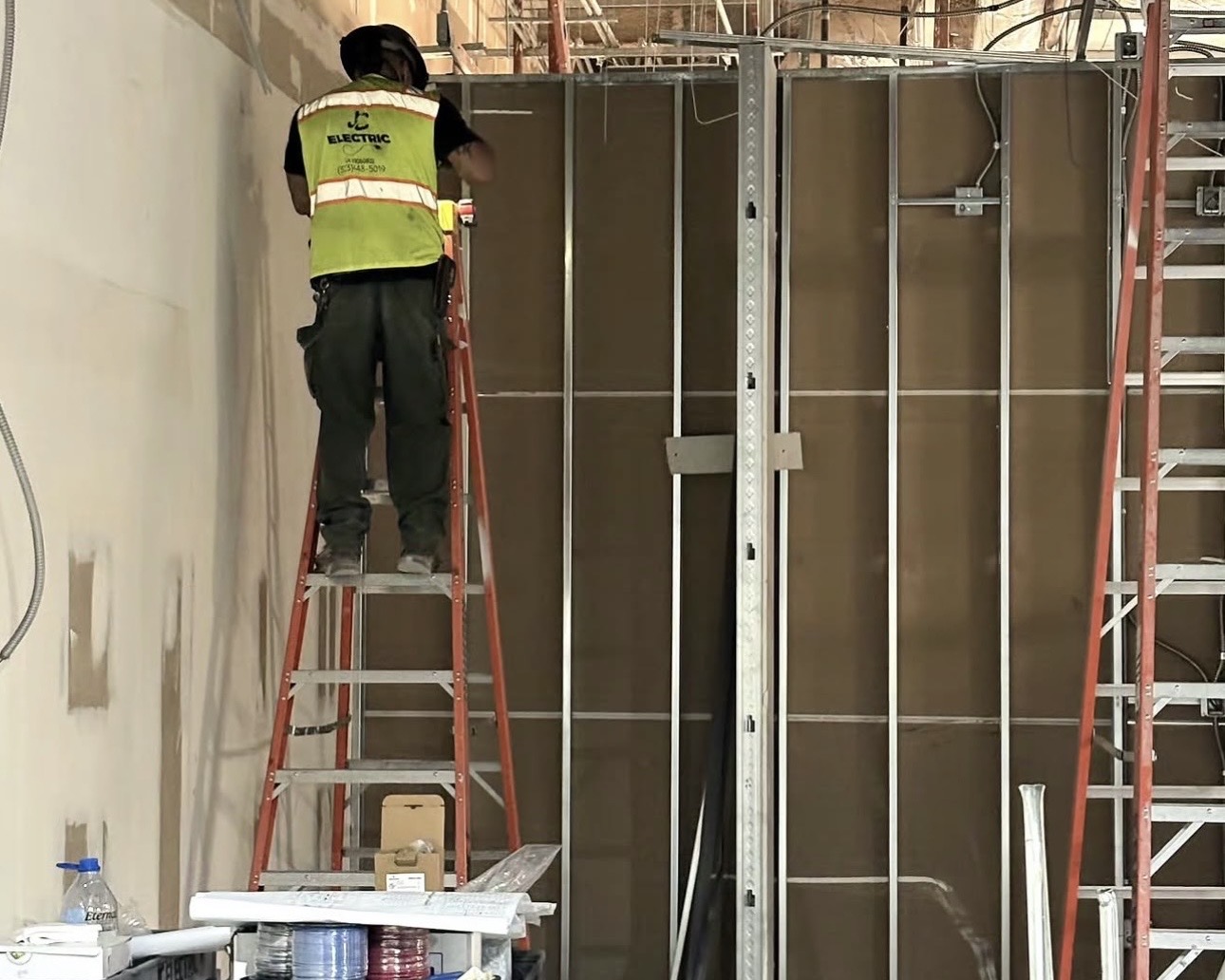 JC Electric technician working from a ladder on a framed commercial wall
